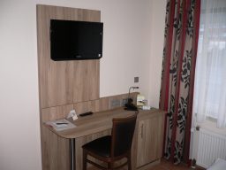 Ein modernes Zimmer mit einem Schreibtisch, Stuhl und einem Fernseher an der Wand.