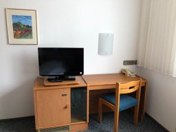 Ein einfaches Zimmer mit Fernseher, Schreibtisch, Stuhl und Telefon.