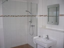 Moderne Badezimmer mit Dusche, Waschbecken und Spiegel, helle Fliesen.