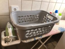 Graue Wäschekorb auf einem Bügelbrett mit Bügeleisen und Waschmittelflaschen.