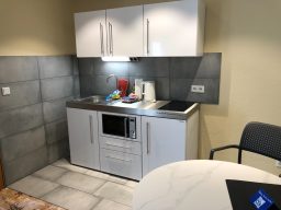 Kleine, moderne Küchenzeile mit Herd, Mikrowelle und Spüle in neutralen Farben.
