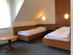 Zwei Einzelbetten in einem hellen Raum mit Holzverkleidung und einer Nachtischlampe.