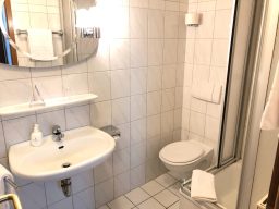 Badezimmer mit Waschbecken, Toilette und Duschkabine in hellem Fliesendesign.