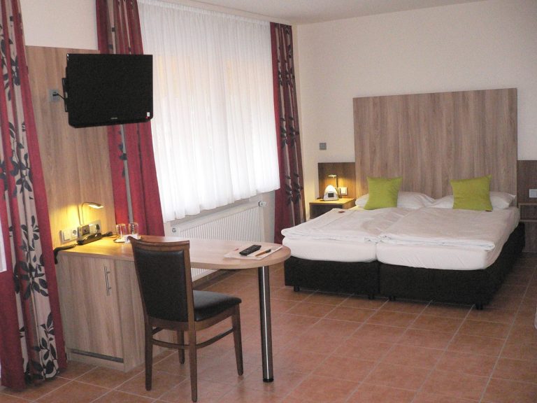 Helle Hotelzimmer mit Doppelbett, Schreibtisch und Fernseher.