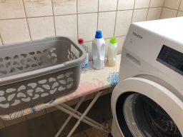 Wäschekorb und Reinigungsmittel neben einer Waschmaschine in einem Raum.