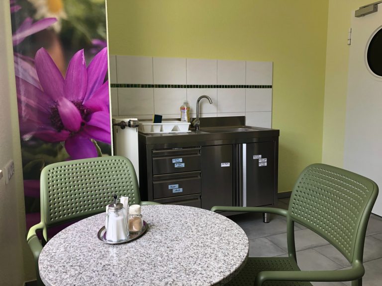 Küchenzeile mit Spüle und Kühlschrank, umgeben von einem Tisch und zwei Stühlen.