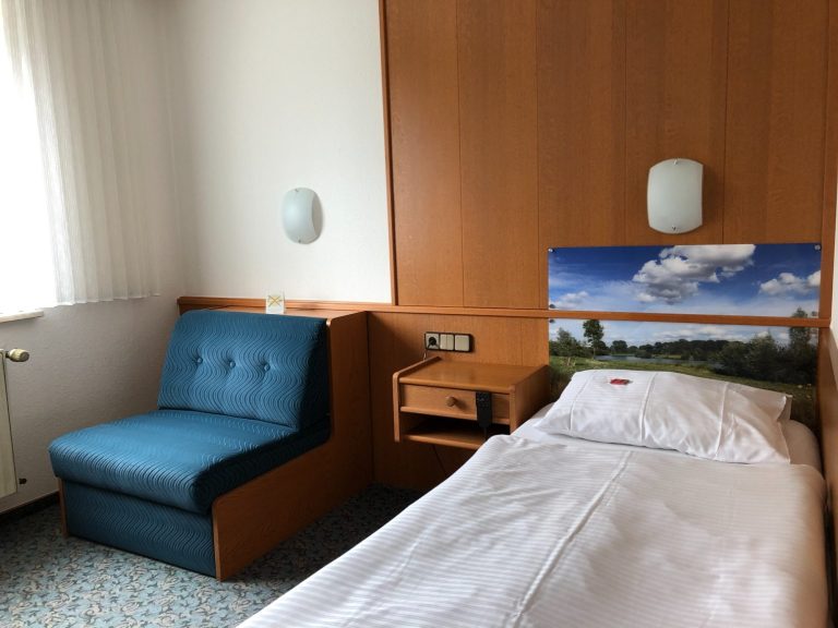 Ein einfaches Einzelzimmer mit einem Bett, einer Sitzecke und holzvertäfelten Wänden.